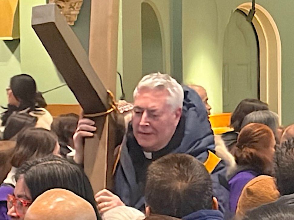 A man carries a wooden cross down an aisle inside a church